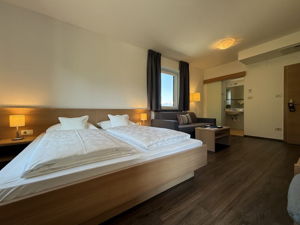 Modernes Hotelzimmer mit Doppelbett, Sofa, Holzmöbeln und Fenster mit Blick auf Berge
