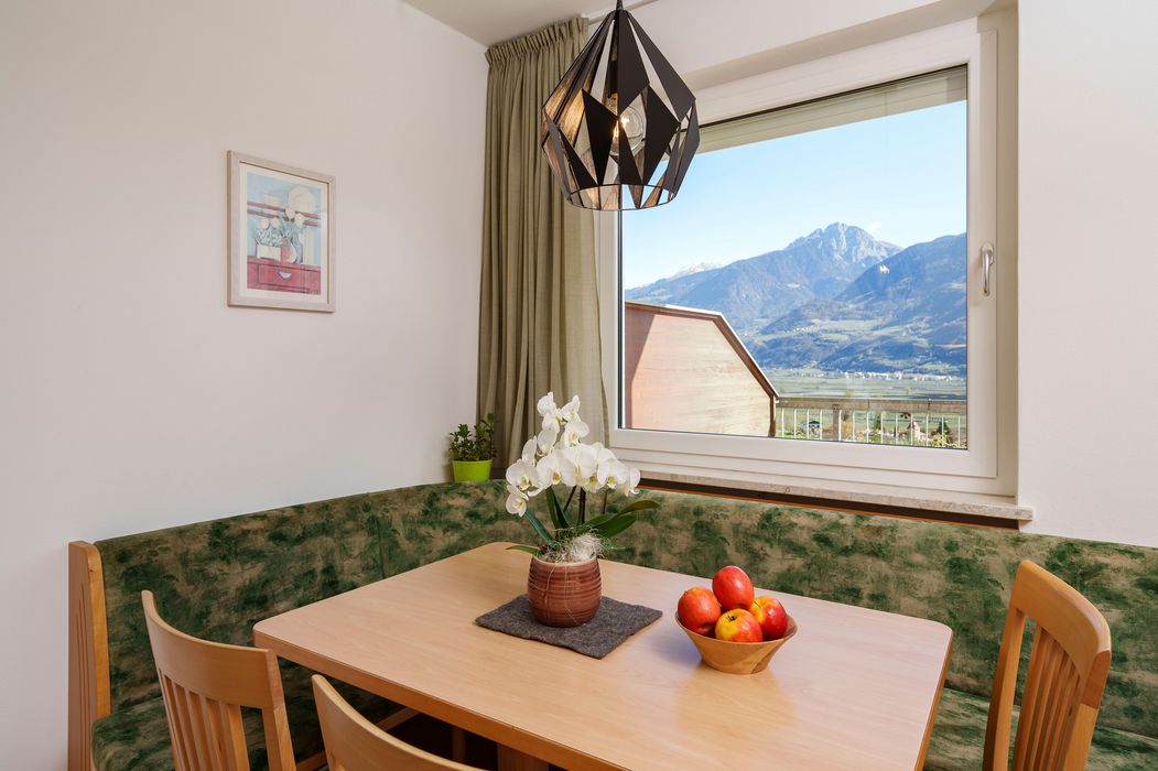 Heller Essbereich mit Holzstühlen, grüner Polsterecke, Orchidee auf dem Tisch und Blick auf Berge durch Fenster