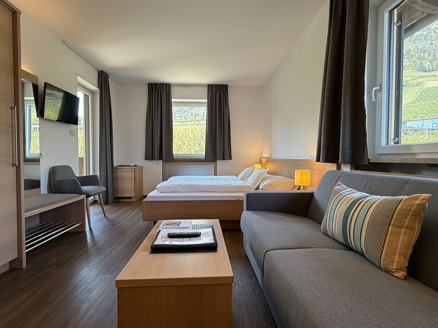 Gemütliches Hotelzimmer mit Bett, Sofa, Couchtisch und Fenster mit Blick auf grüne Hügel