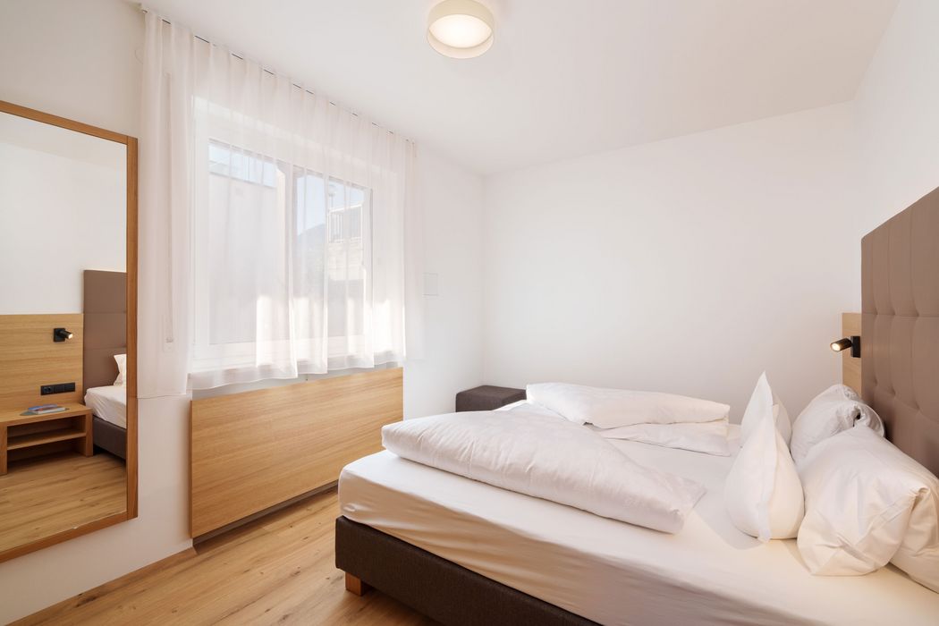 Helles, schlicht eingerichtetes Schlafzimmer mit Doppelbett, Holzboden und großem Spiegel an der Wand.