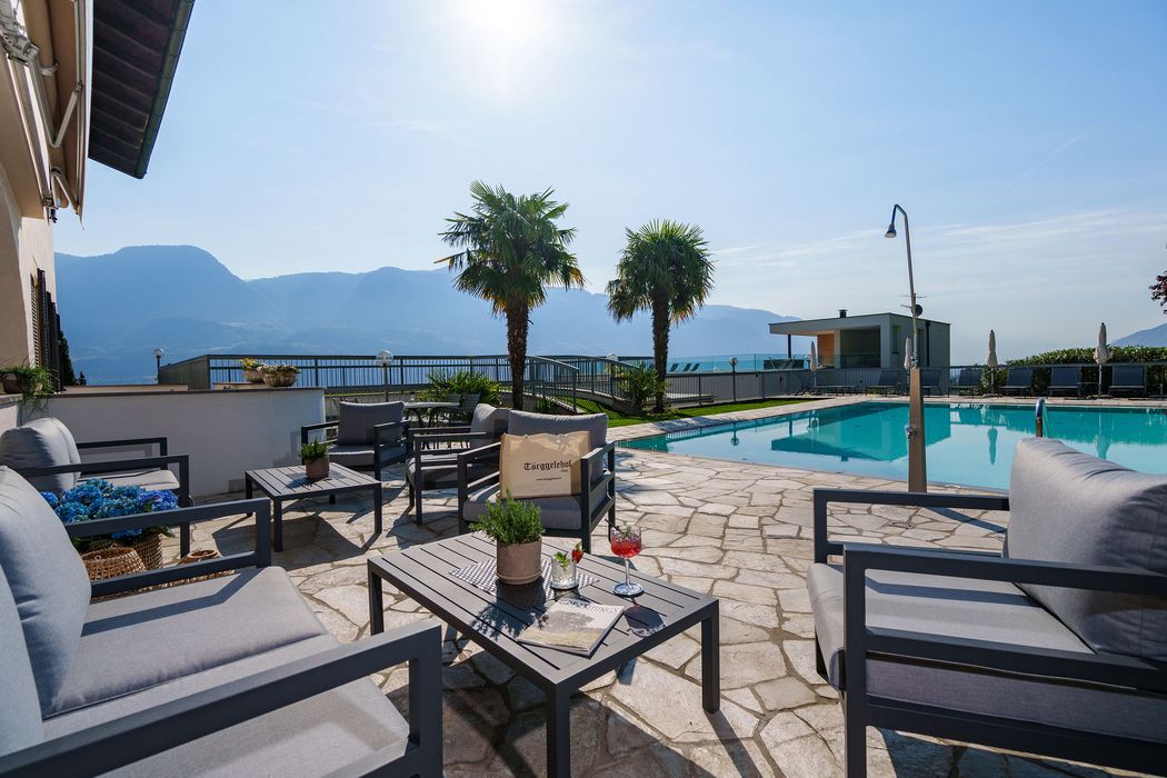 Terrasse mit Sitzgruppen, Pool, zwei Palmen und Bergblick bei sonnigem Wetter