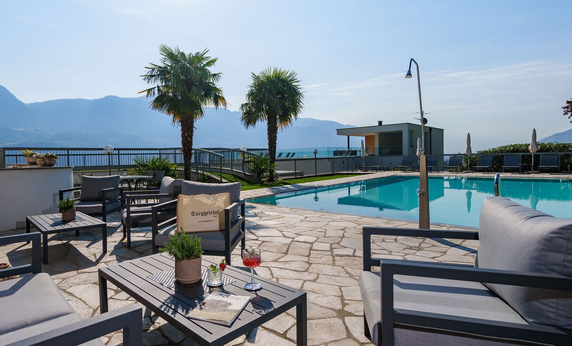 Terrasse mit Sitzgruppen, Pool, zwei Palmen und Bergblick bei sonnigem Wetter