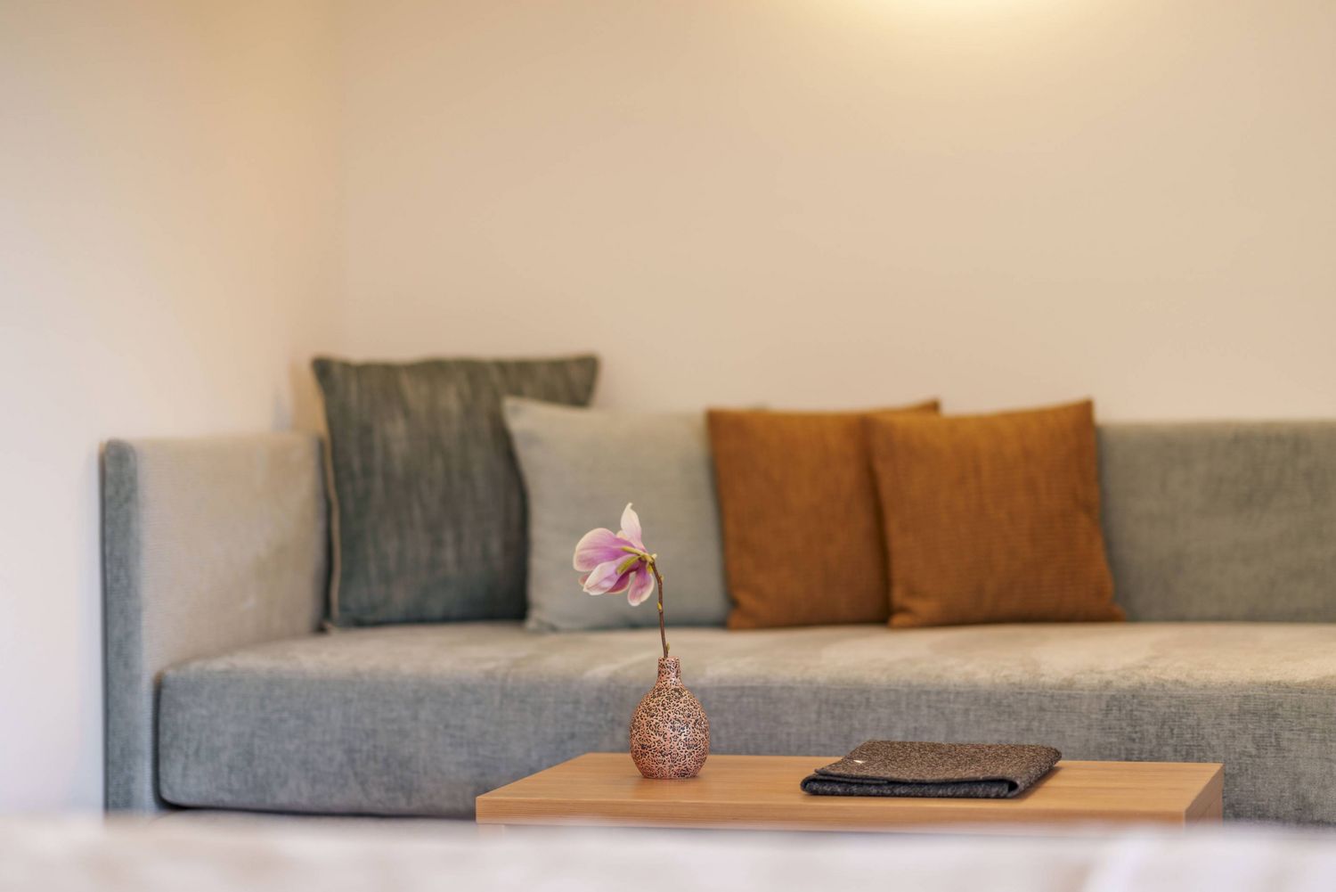 Gemütliches Wohnzimmer mit grauem Sofa, bunten Kissen und kleinem Tisch mit Blumenvase