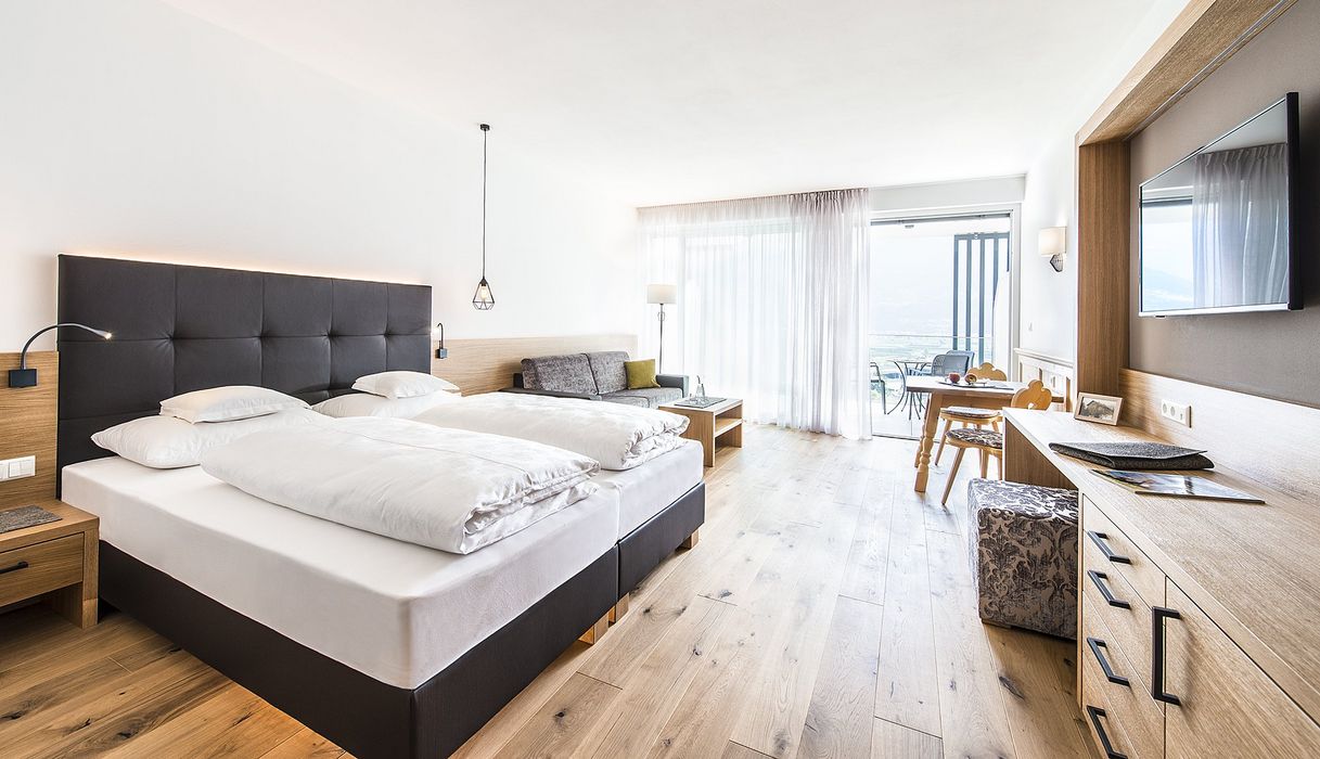 Modernes, helles Hotelzimmer mit zwei Einzelbetten, Sofa, Holzmöbeln und Balkon mit Aussicht