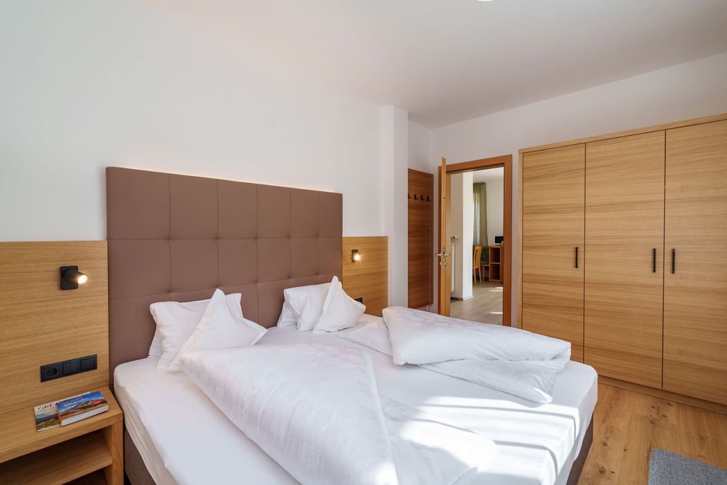 Modernes Schlafzimmer mit weißem Bett, braunem Polsterkopfteil und großem Holzschrank