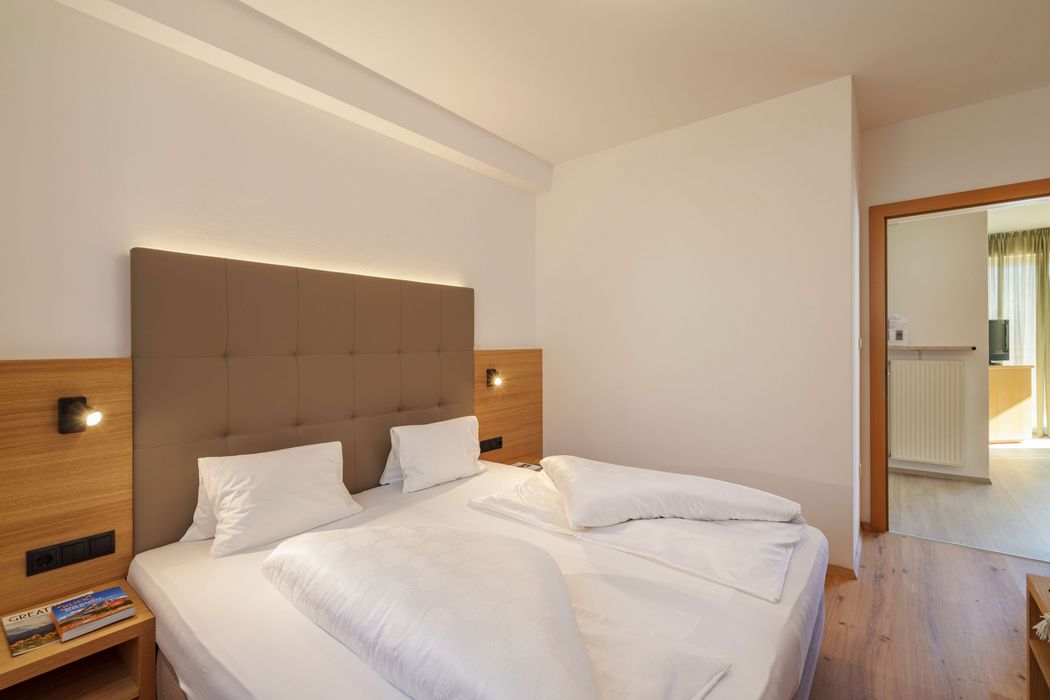 Modernes Schlafzimmer mit einem Doppelbett, Kopfteil mit Beleuchtung und offenem Türrahmen zum angrenzenden Raum